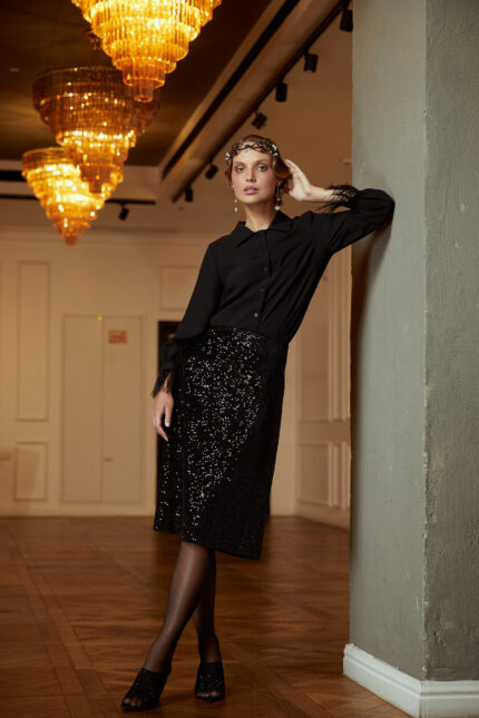 דוגמנית מציגה חצאית ערב צנועה וחולצה צנועה חגיגית בצבע שחור עם סיומת נוצות בשרוול